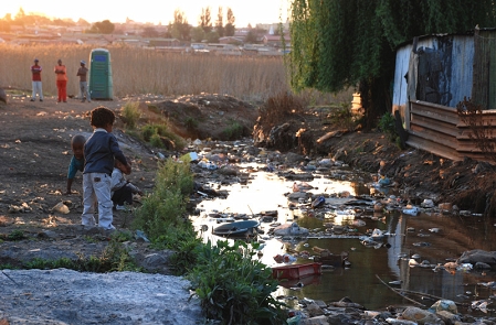 Kinder spielen an einem vermüllten Fluss in Südafrika